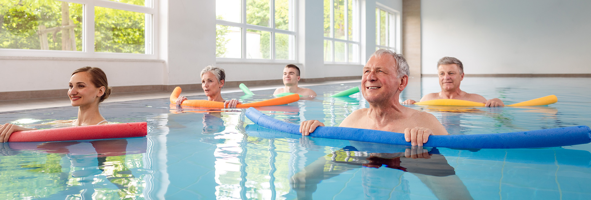 Kur: Ältere und jüngere Menschen im Schwimmbecken mit bunten Schwimmnudeln