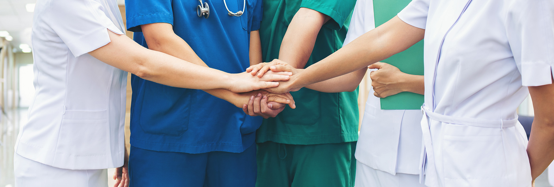 Team aus Ärztinnen:Ärzten und Pfleger:innen legen Hände übereinander