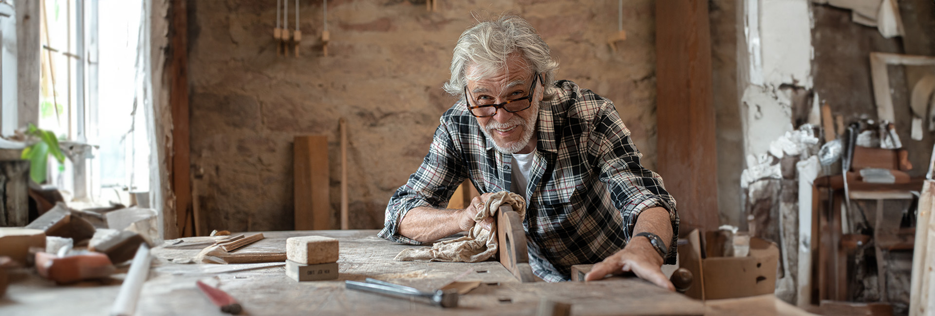 Älterer Mann in Pension arbeitet in Werkstatt an Hobelbank