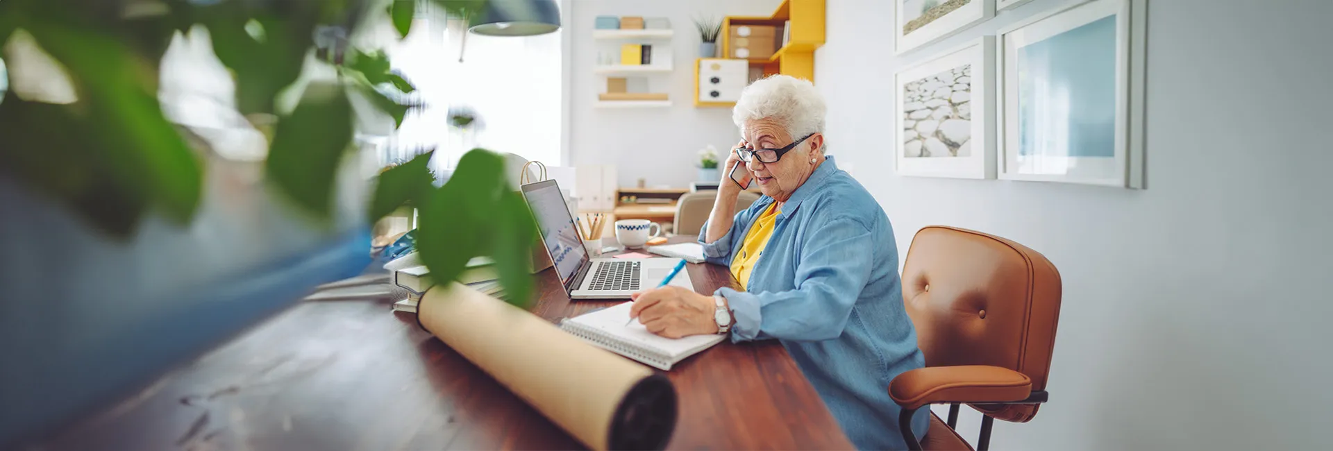 Seniorin am Schreibtisch telefoniert und notiert sich Auskunft zur Meldepflicht