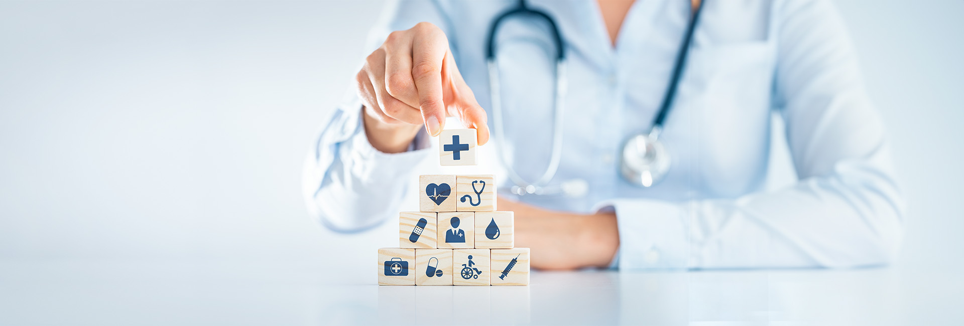 Krankenversicherung: Ärztin stapelt Holzbausteine mit Gesundheitssymbolen
