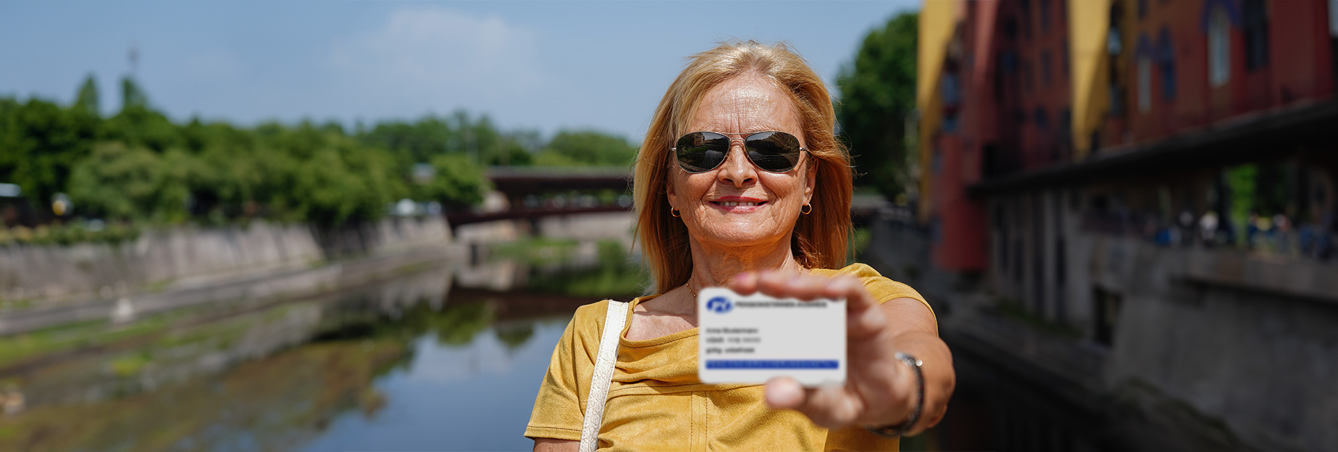 Ältere Frau mit Sonnebrille zeigt ihren Ausweis für Pensionist*innen im Scheckkartenformat